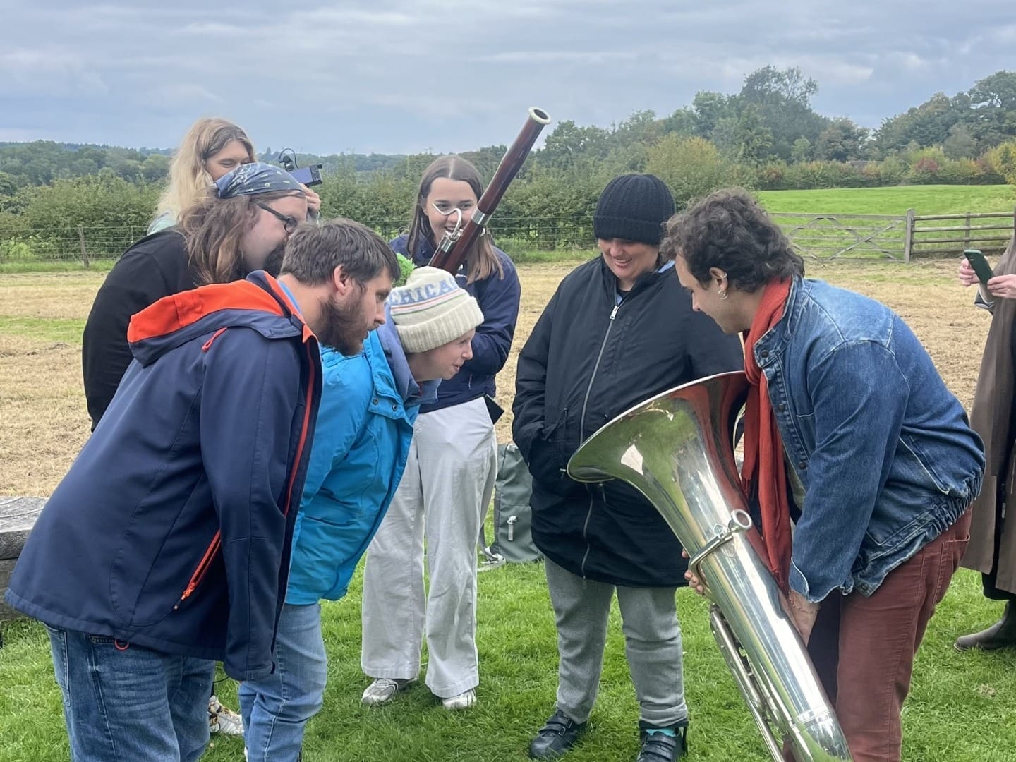 A group of adults including a tuba player and bassoonist outdoors looking at a large paper on the ground