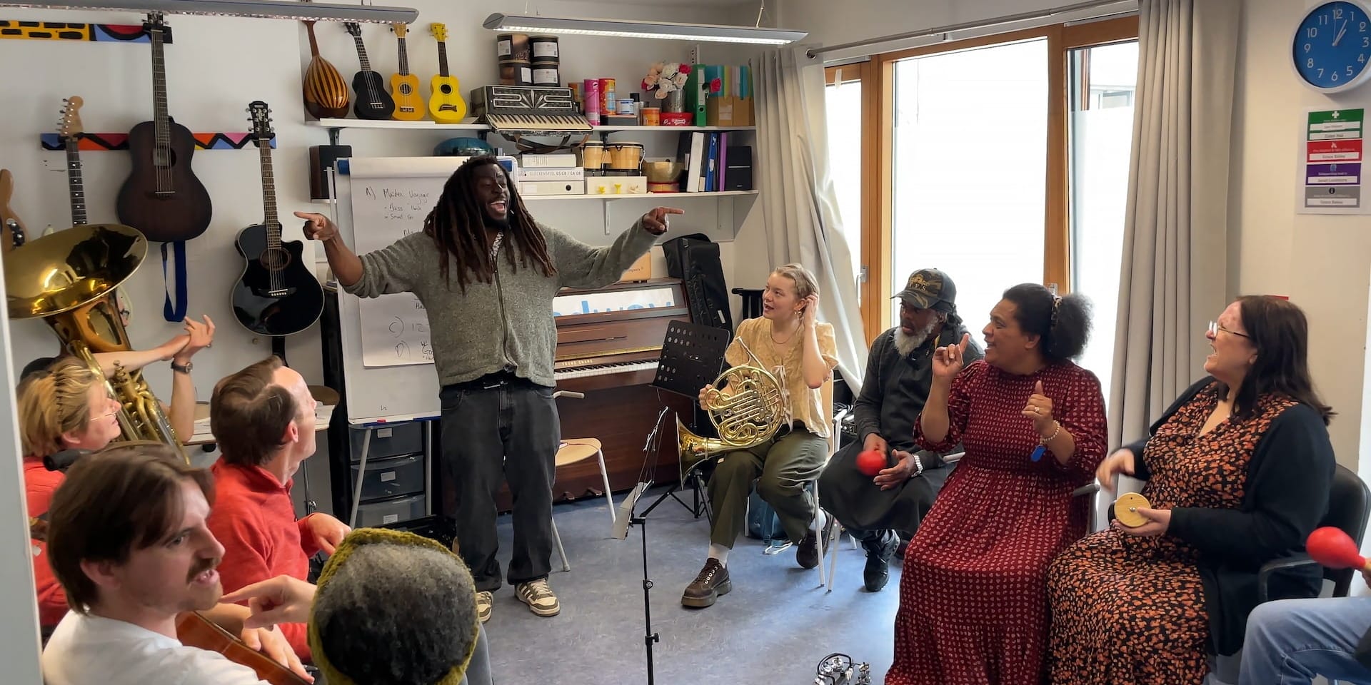 Participants in the LPO's musical project with Headway sit in a circle watch the presenter smiling and spreading his arms wide to either side of him