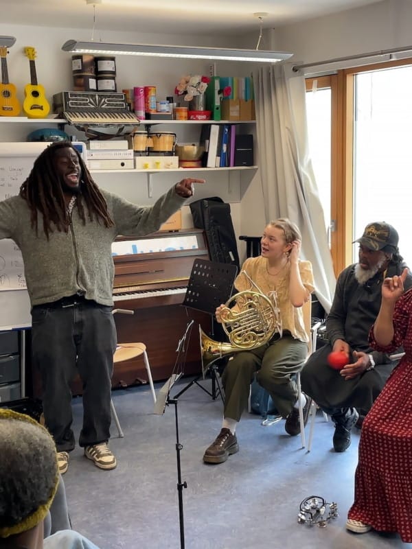 Participants in the LPO's musical project with Headway sit in a circle watch the presenter smiling and spreading his arms wide to either side of him