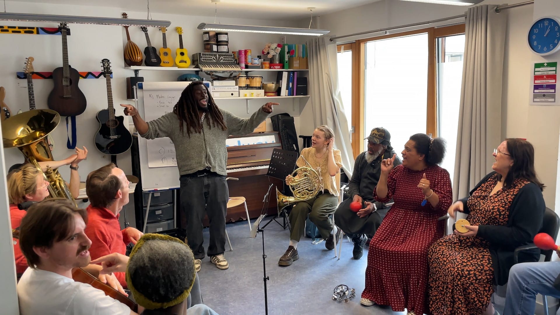 Participants in the LPO's musical project with Headway sit in a circle watch the presenter smiling and spreading his arms wide to either side of him