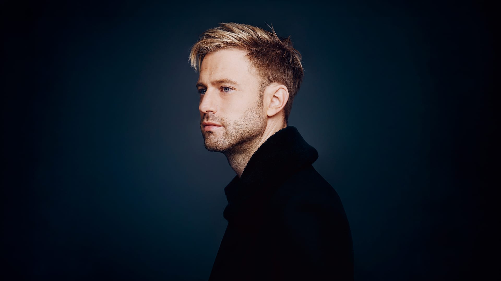 Baritone Benjamin Appl, a man with short blond hair, wearing a dark jacket, formal portrait.