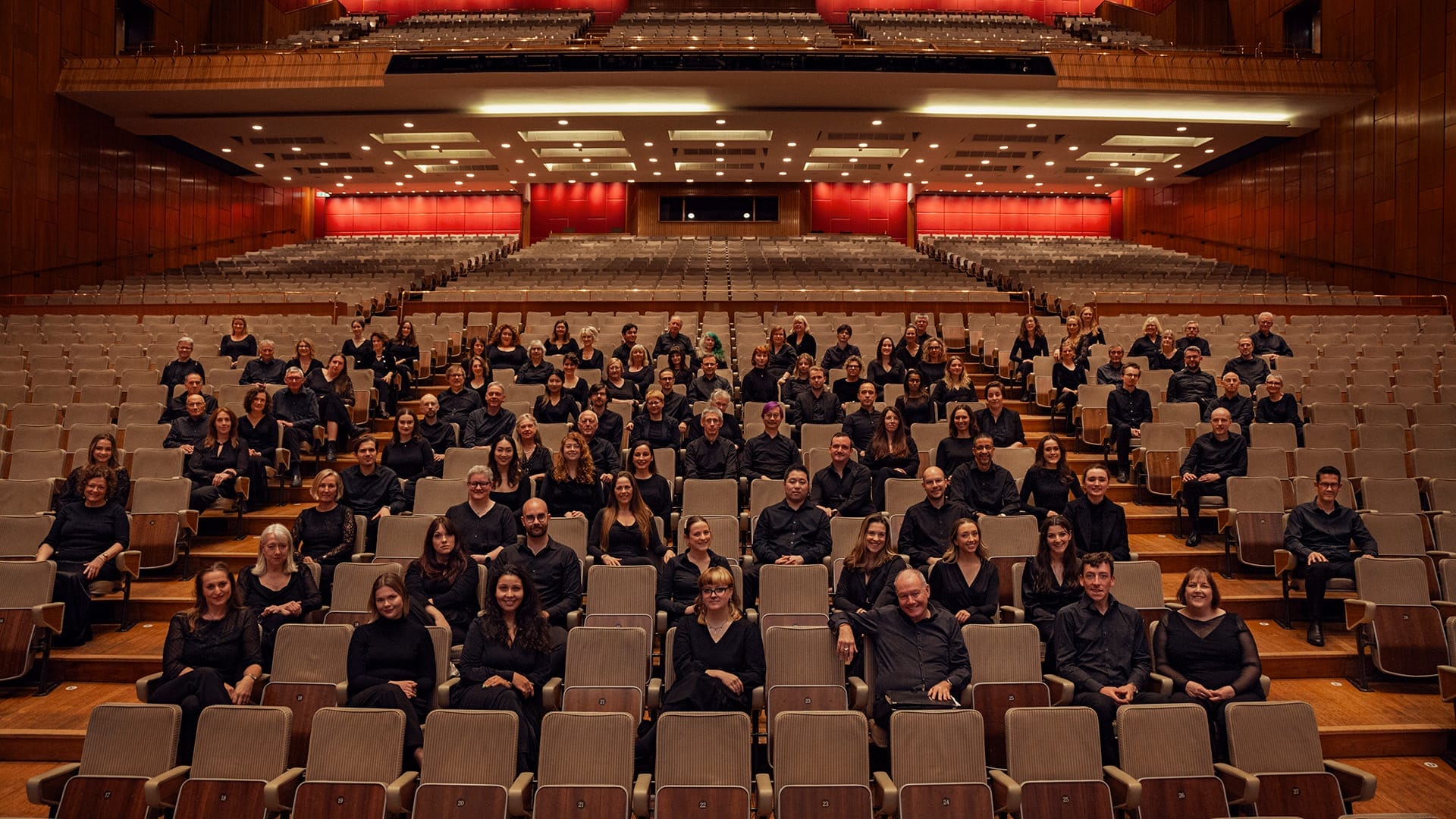 Members of the London Philharmonic Choir seated in a concert hall auditorium looking at the camera.