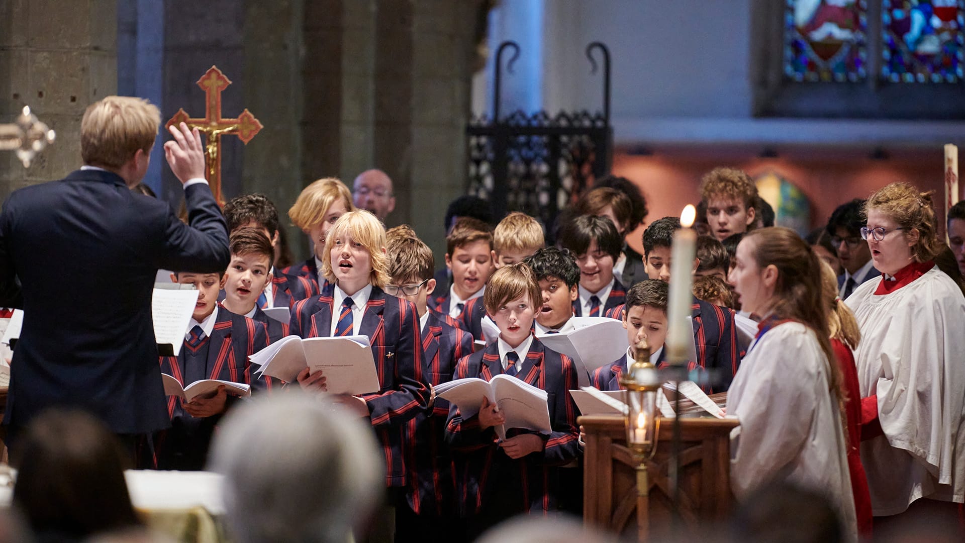 Choristers from the Tiffin Choirs wearing school uniform singing from songbooks in a church.