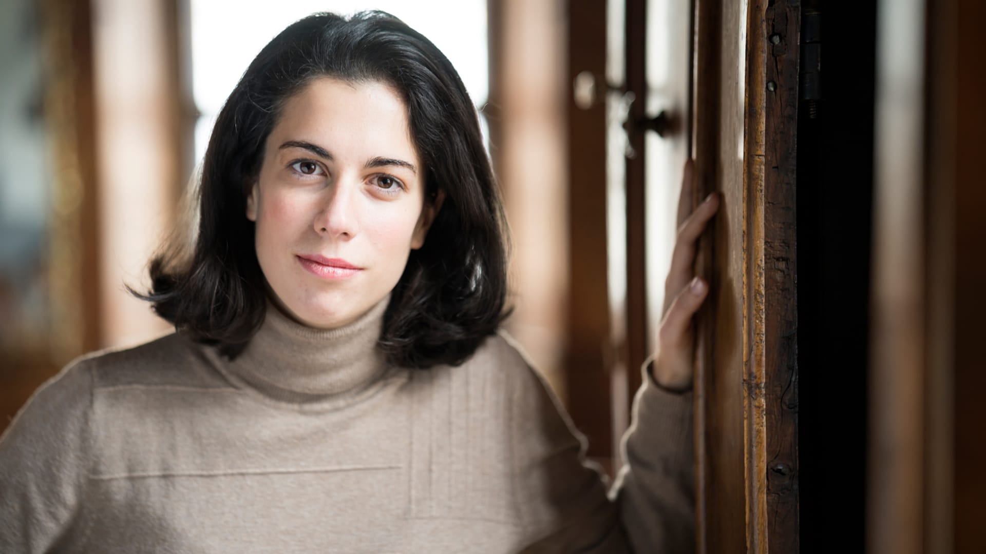 Conductor Marie Jacquot, a woman with short dark hair, wearing a beige turtleneck, gently smiling at the camera.