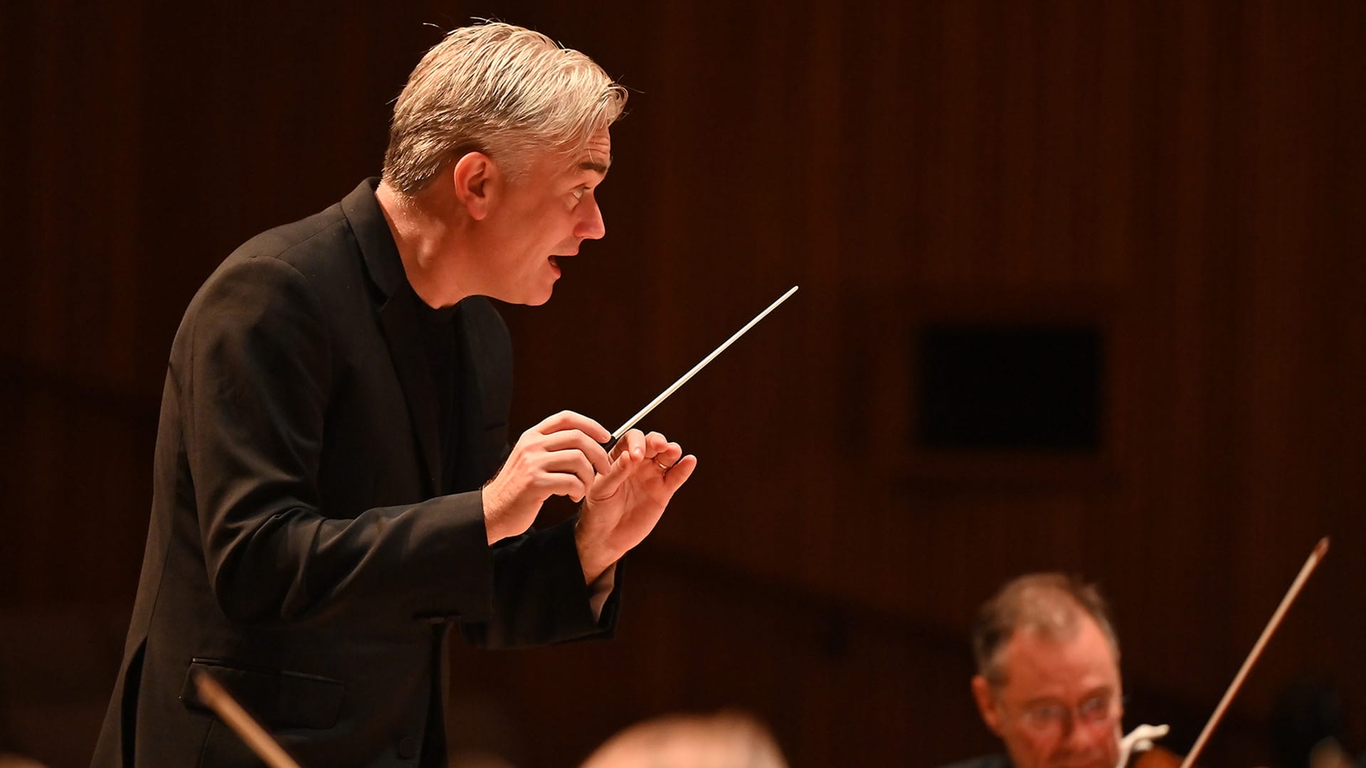 Conductor Edward Gardner, a man with short silver hair, colour portrait in a conducting pose.