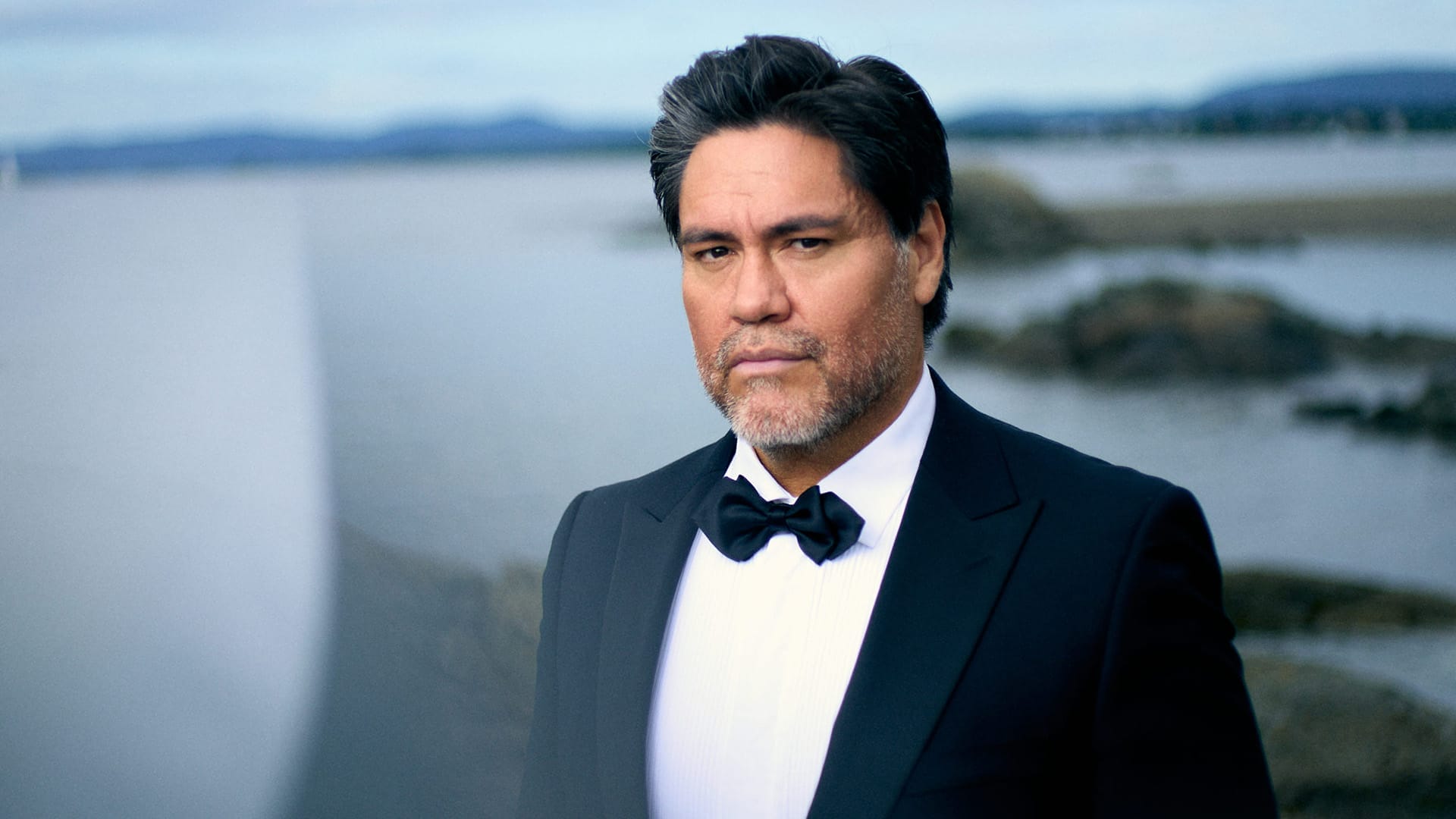 Bass-baritone Yngve Søberg, a man with black hair wearing a tuxedo, ocean and rocky background, formal portrait.