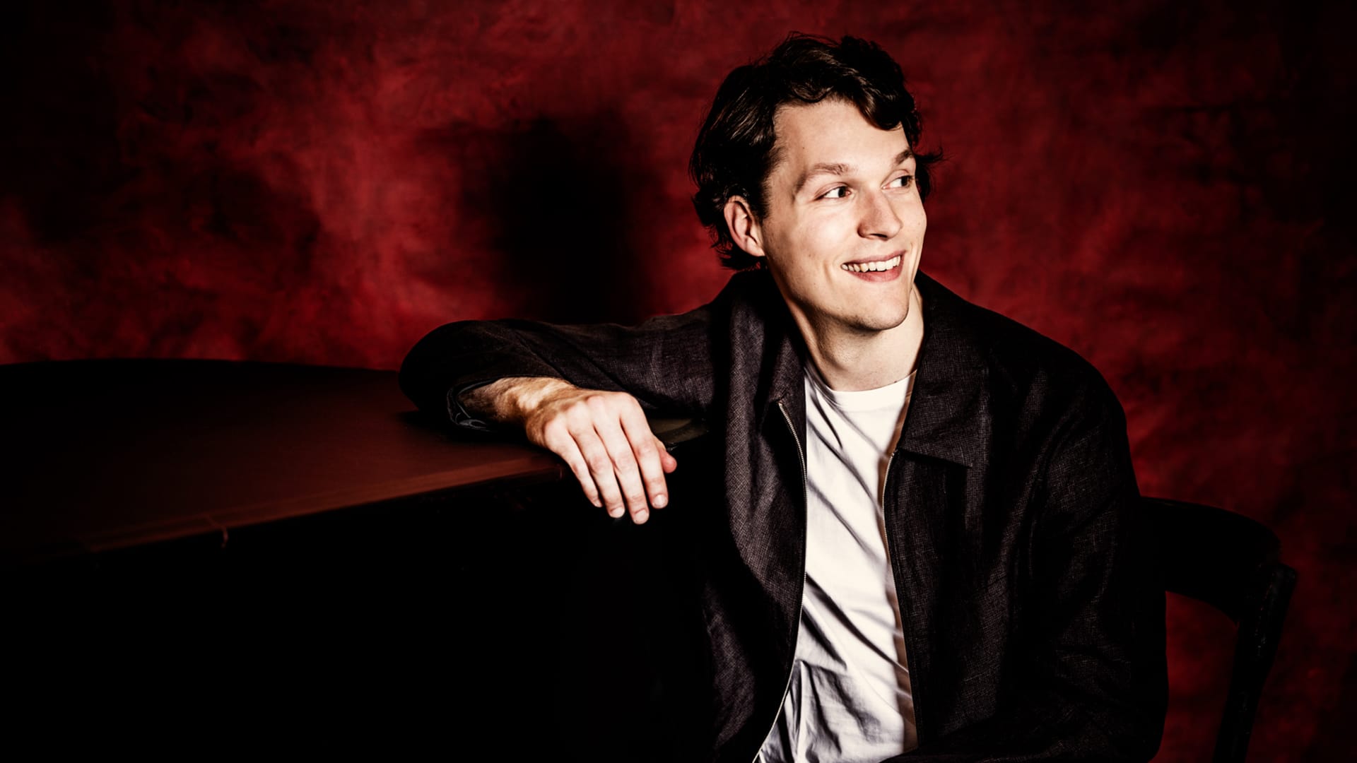 Pianist Lukas Sternath smiles and rests his arm on a piano.