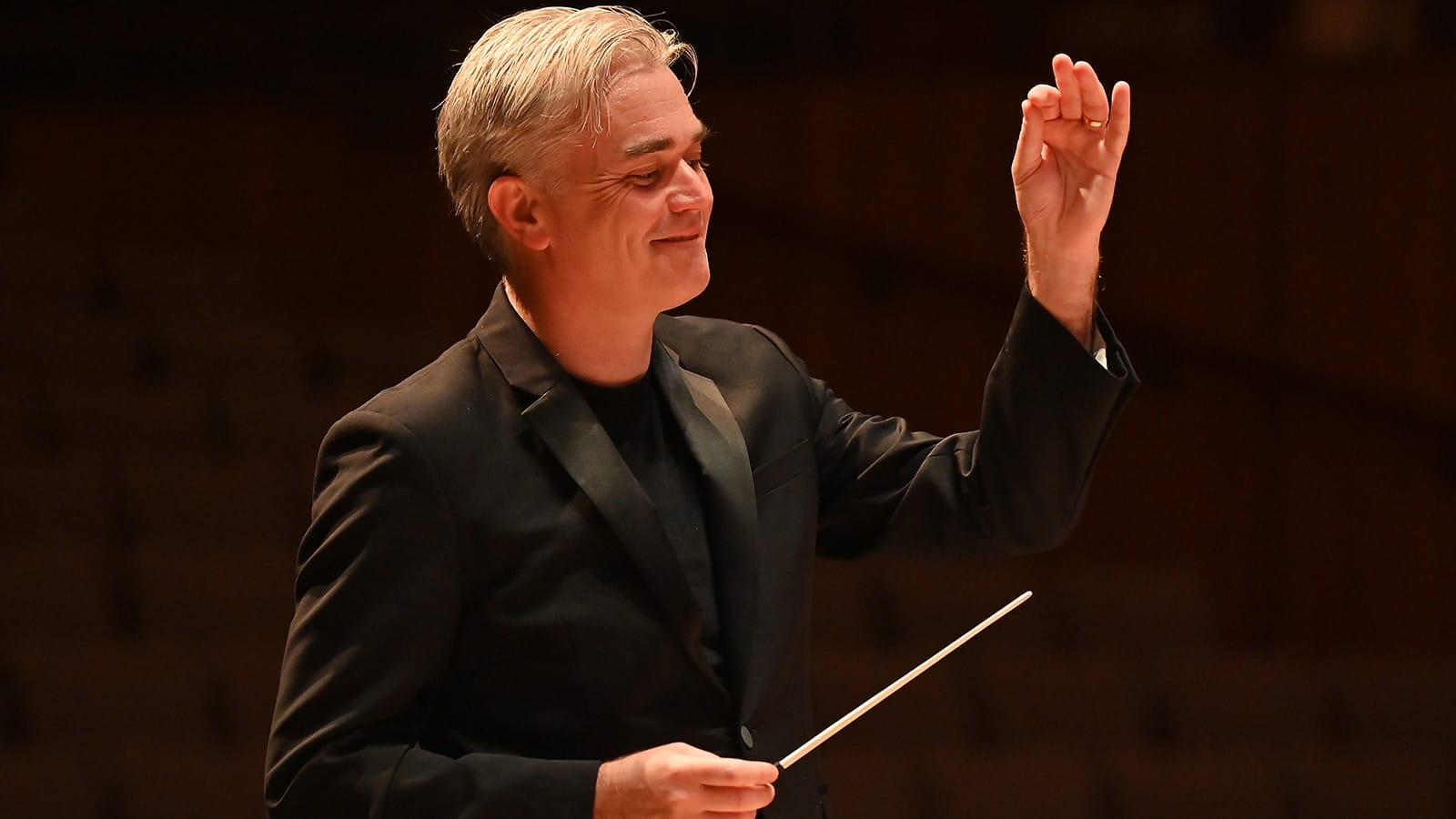Conductor Edward Gardner, a man with short silver hair, colour portrait in a conducting pose.