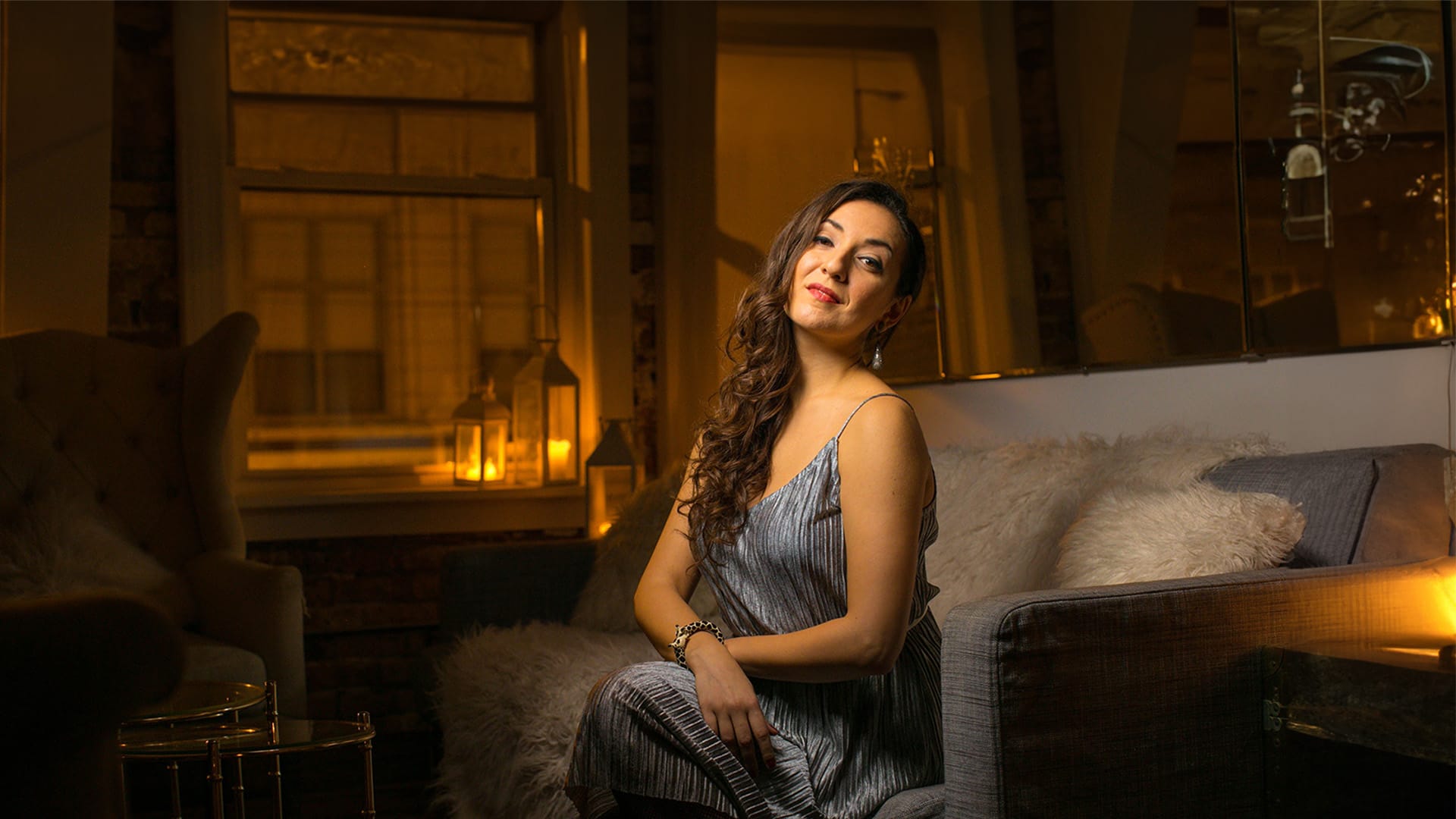 Soprano Rosa Feola, a woman with long brown, curled hair, looks at the camera whilst seated on a fur-lined sofa.