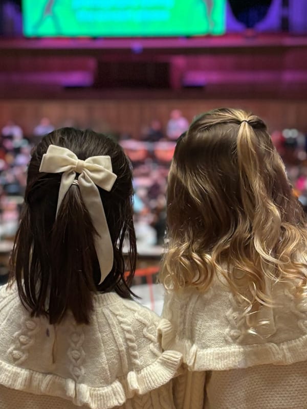 Two young girls with bows in their hair watching the FUNharmonics performance in the Royal Festival Hall.