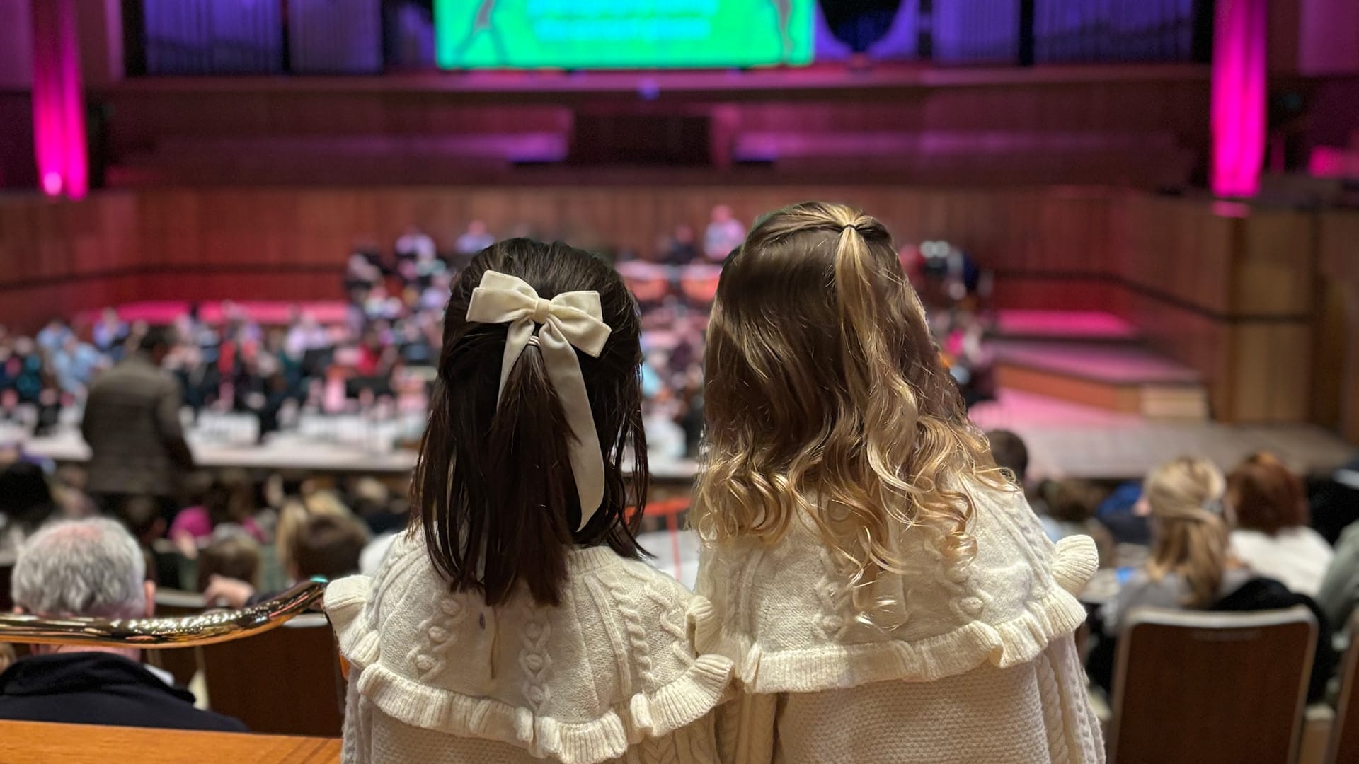 Two young girls with bows in their hair watching the FUNharmonics performance in the Royal Festival Hall.