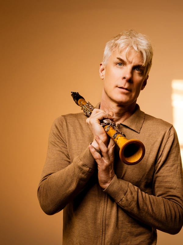 Clarinettist Martin Fröst poses with his clarinet against an orange wall.